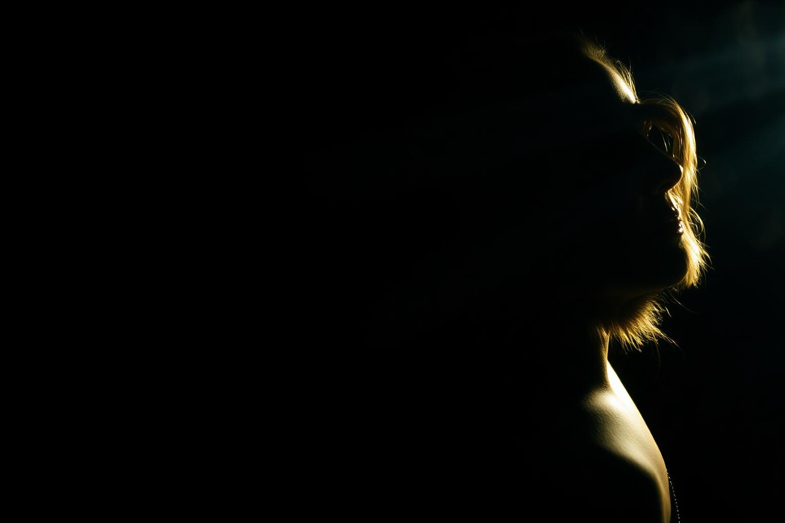 Cinematic film-still portrait of Toronto bilingual actor Ghazaleh Ghasemi in profile, carved from a deep black background by a single warm rim light, 35mm film aesthetic with subtle smoke.